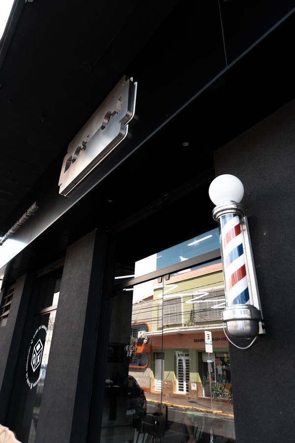 Entrada da barbearia com poste de barbeiro tradicional